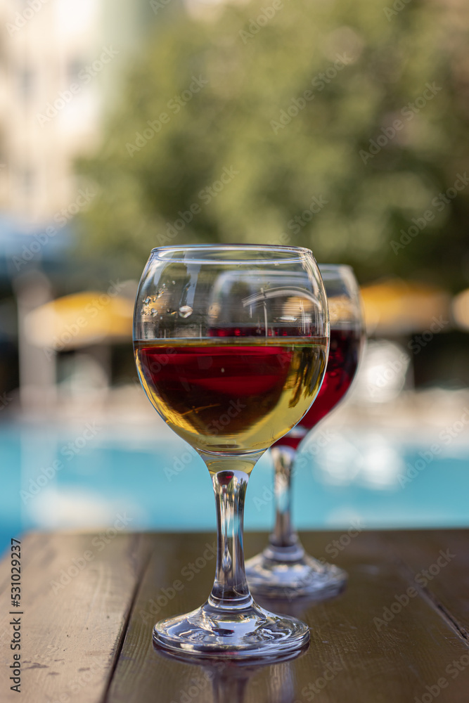 Two glasses of wine on a wooden table next to the swimming pool in summer. Relaxing vacation, holiday and happy weekend concept. Two glasses of wine on a wooden table next to the swimming pool in summer. Relaxing vacation, holiday and happy weekend concept.