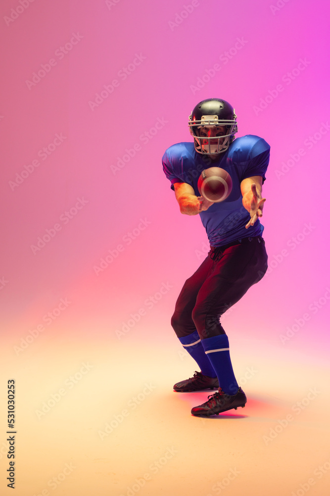 Caucasian male american football player holding ball with neon pink lighting