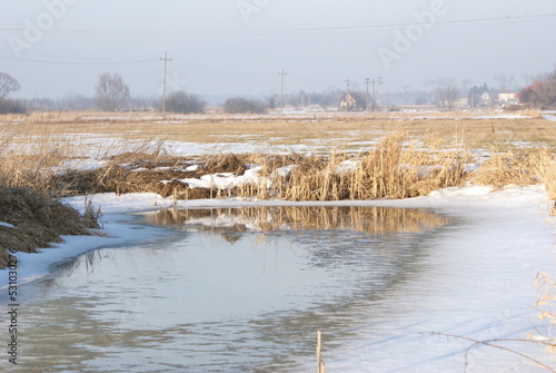 Frozen pond in the meadow. Winter time with snow on fields.