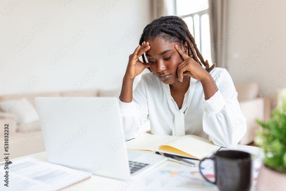 Exhausted businesswoman having a headache in home office. African American creative woman working at office desk feeling tired. Stressed business woman feeling eye pain while overworking Exhausted businesswoman having a headache in home office. African American creative woman working at office desk feeling tired. Stressed business woman feeling eye pain while overworking