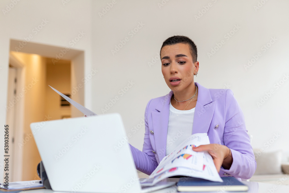 Fototapeta premium Remote job, technology and people concept - happy smiling young business woman with laptop computer and papers working at home office during the Covid-19 health crisis.