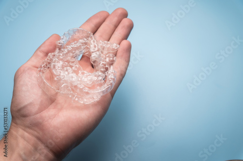 Close-up of a man holding invisible aligners for whitening and straightening his teeth on a blue background. Orthodontic treatment instead of or after braces © yanik88