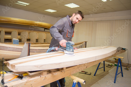 Young carpenter making wooden boat of his own design in his workshop