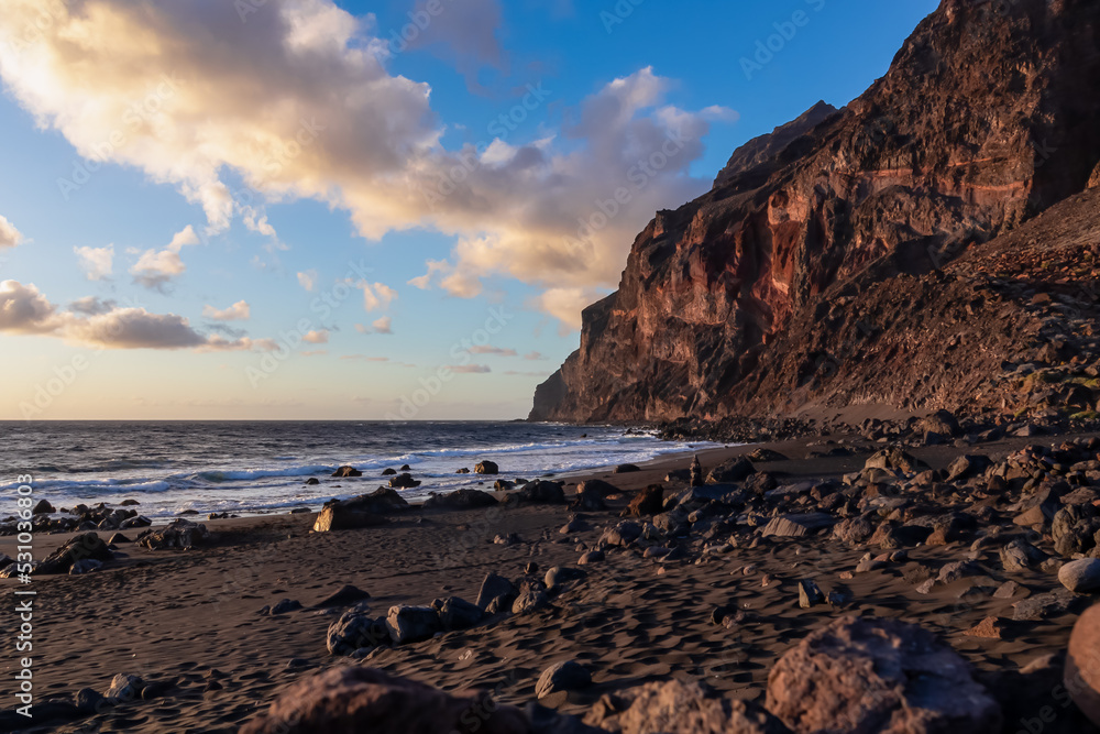 Scenic view during sunset on the volcanic sand beach Playa del Ingles in Valle Gran Rey, La Gomera, Canary Islands, Spain, Europe. Massive cliffs of the La Mercia range. Calm atmosphere at the seaside