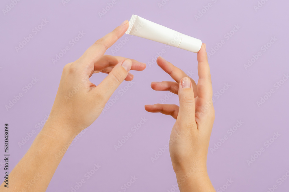 Hand holds plastic cream battle isolated on lilac background. Beauty concept. Packaging tube for cosmetic products Hand holds plastic cream battle isolated on lilac background. Beauty concept. Packaging tube for cosmetic products