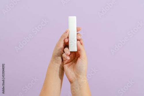 Cosmetic cream battle in womans hand on light lilac background. Beauty concept. Packaging tube for cosmetic products