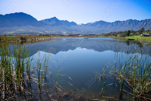 A lake, with water reeds, nestles in a bowl of magnificent mountains and wine lands in a serene valley near Tulbagh in the Western Cape.