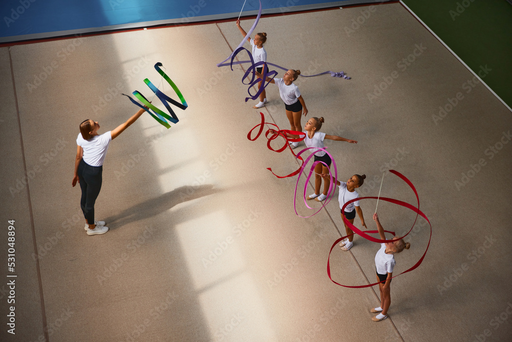 © master1305 - Aerial view. Female sports coach training gymnastics athletes at sports gym, indoors. Concept of sport, studying, art, education