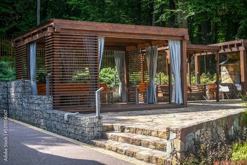 Foto Close up wooden gazebo decorated with gabion elements and natural stone pavement