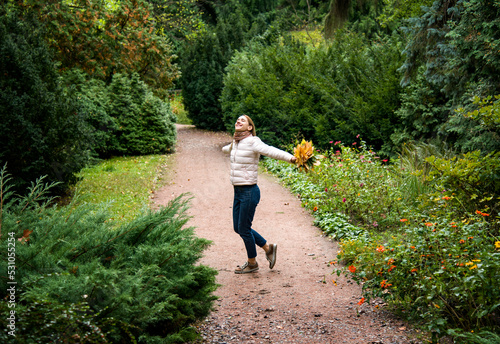 beautiful smiling girl in pink sport jacket walking in autumn park with a bouquet of autumn leaves holding in her hands © Tetatet