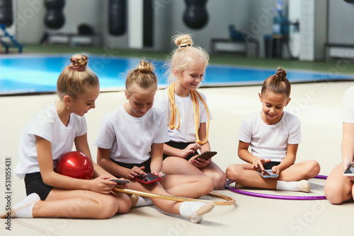 Happy kids, beginner gymnastics athletes having rest after sports training at sports gym, indoors. Concept of sport, studying, art, education