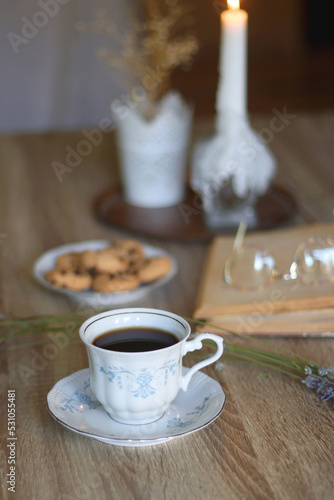 Fototapeta Naklejka Na Ścianę i Meble -  Cup of tea, plate with chocolate chip cookies, open book, reading glasses, lit candles and dry lavender flowers. Hygge at home, selective focus.