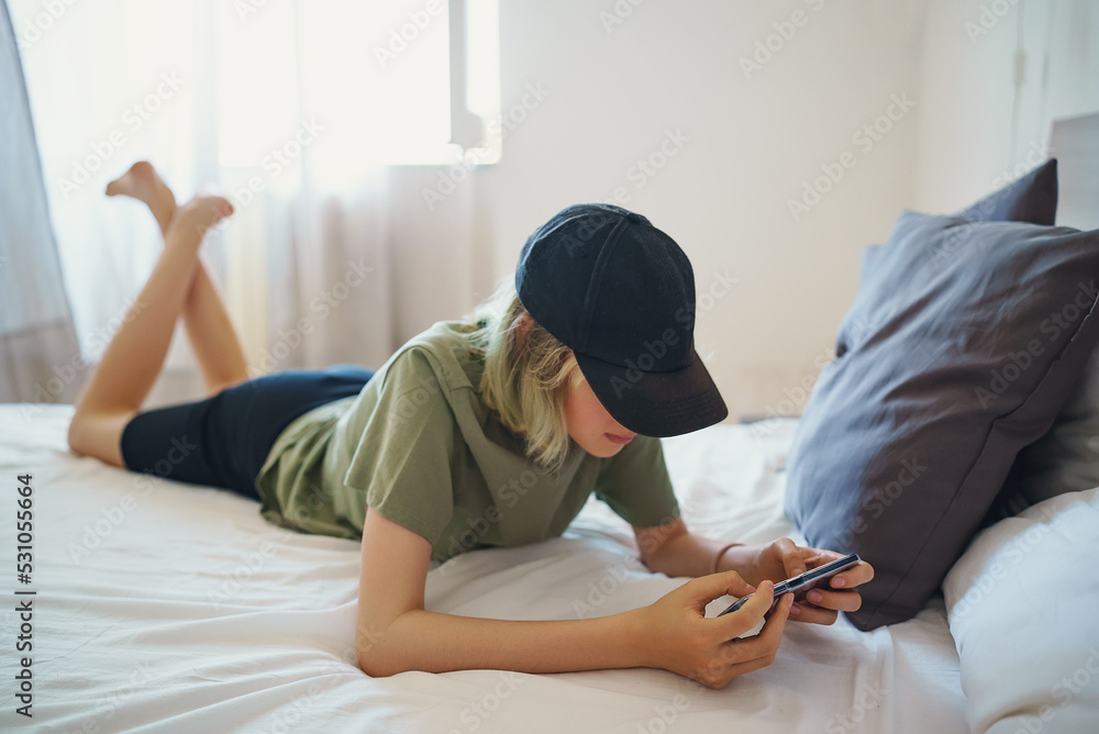 Teenager lies with smartphone on the bed. Concept of gadget addiction.