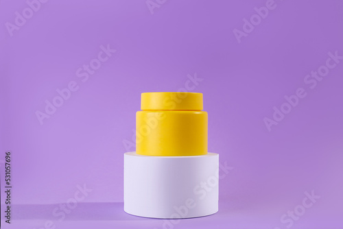 Yellow jar of cream on a stand, white podium on a purple background. Stylish look of the product, mock up, identity..