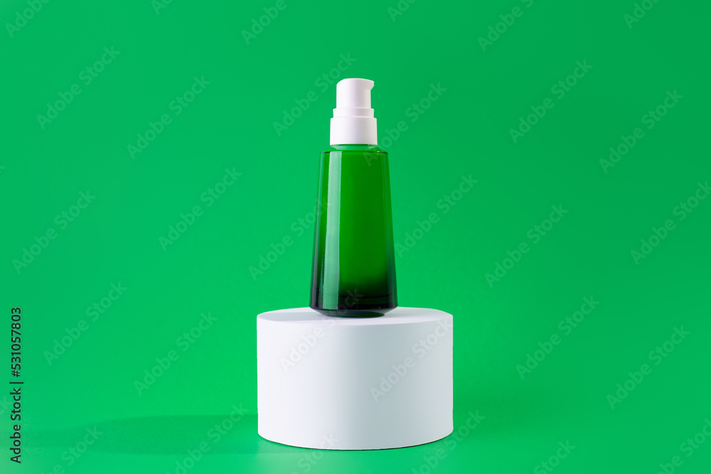 Green, glass bottle of cream or serum on a stand, white podium on green background. Design Template of Fashion Cosmetics Product for Ads, flyer, banner or Magazine Background. Green, glass bottle of cream or serum on a stand, white podium on green background. Design Template of Fashion Cosmetics Product for Ads, flyer, banner or Magazine Background.