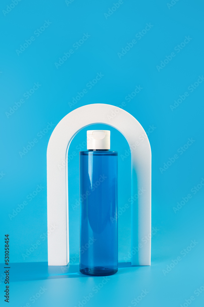 Micellar water or toner bottle for facial skin care. Cosmetic care product in a glass shade on the blue background of white arches. Copy space.. Micellar water or toner bottle for facial skin care. Cosmetic care product in a glass shade on the blue background of white arches. Copy space..