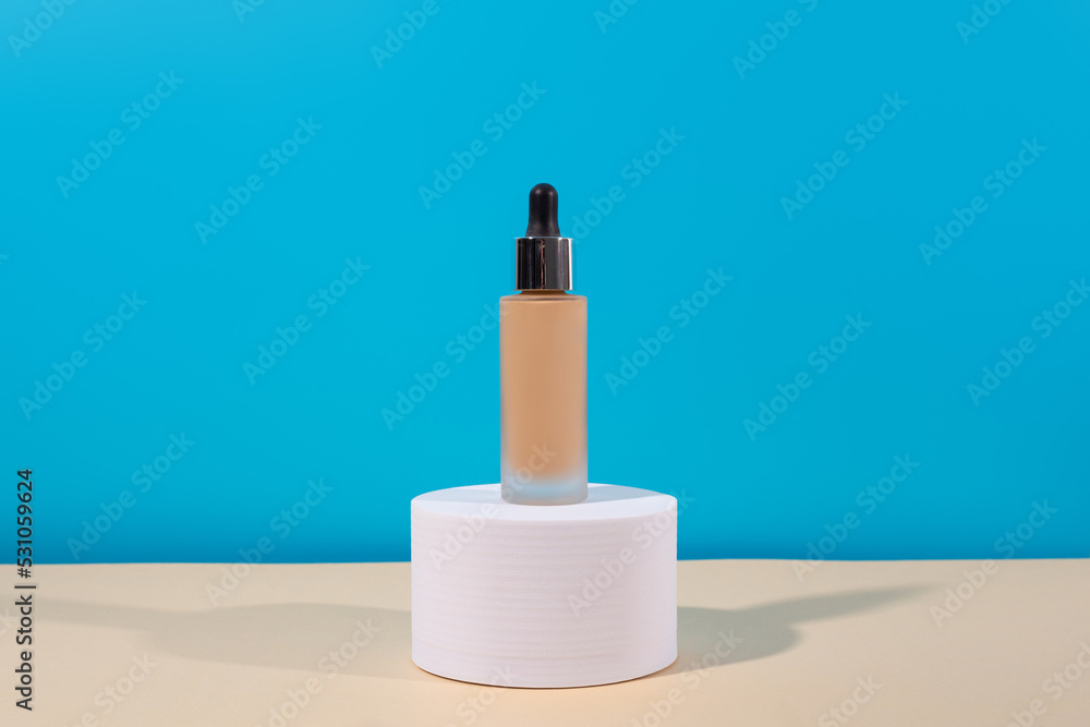 Bottle with foundation liquid beige cream on stand, white podium. Professional makeup product for perfect complexion. Woman accessories, base beauty product, primer, concealer. Bottle with foundation liquid beige cream on stand, white podium. Professional makeup product for perfect complexion. Woman accessories, base beauty product, primer, concealer.