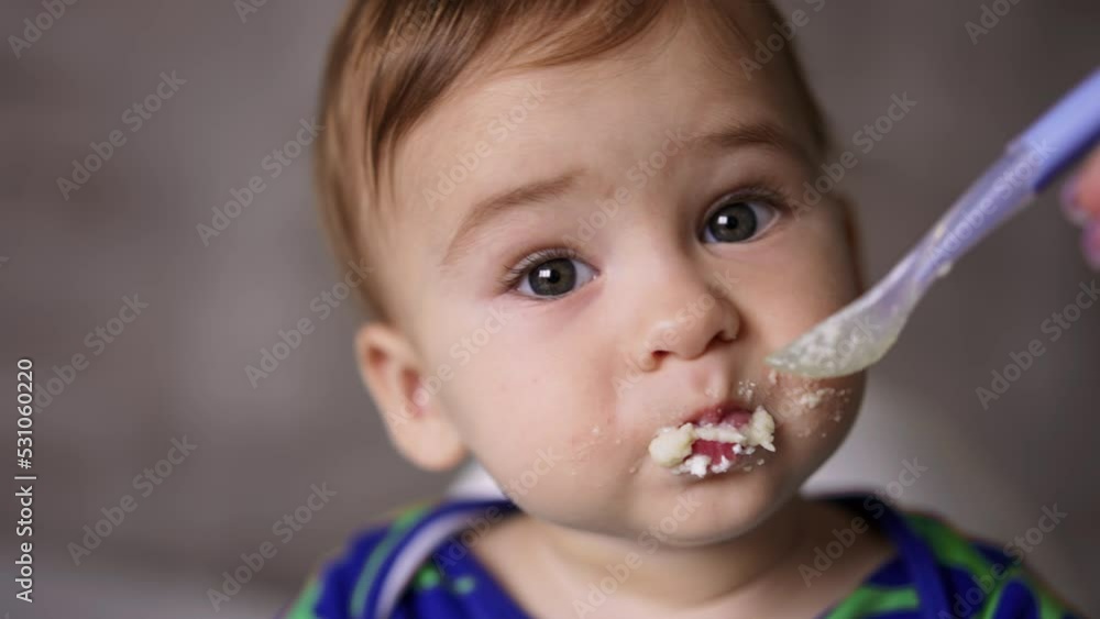 Sweet little kid nutrition. Mom gives a spoon with food to her child and cleans his mouth. Close up. Blurred backdrop. Sweet little kid nutrition. Mom gives a spoon with food to her child and cleans his mouth. Close up. Blurred backdrop.