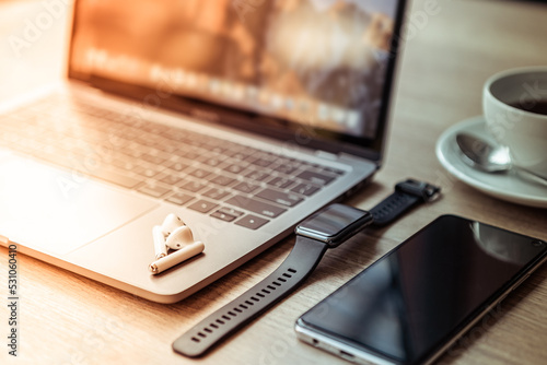 Close-up of Keyboard laptop computer, wireless earphones focus with smartwatch and smartphone empty screen on wooden background office desk in coffee shop like the background