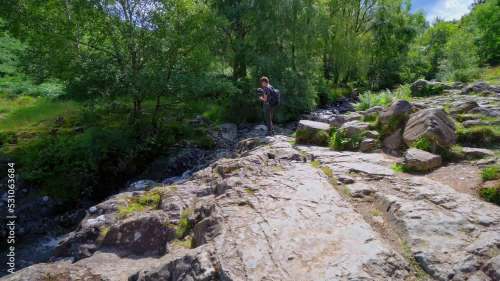 Young boy photographing a slow moving woodland stream with ferns on the riverbank and water flowing over the rocks. Shot in the Lake District England. Young boy photographing a slow moving woodland stream with ferns on the riverbank and water flowing over the rocks. Shot in the Lake District England.