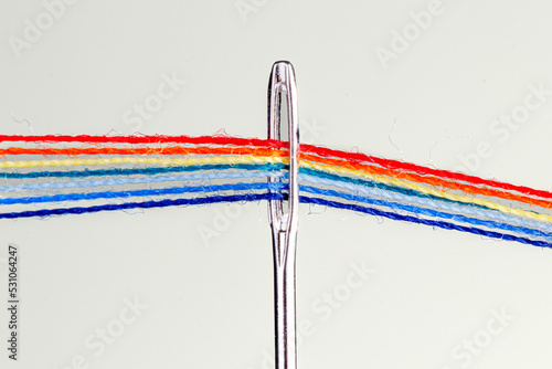 multi-colored threads for sewing in the form of a rainbow pass through an antique needle on a white background photo