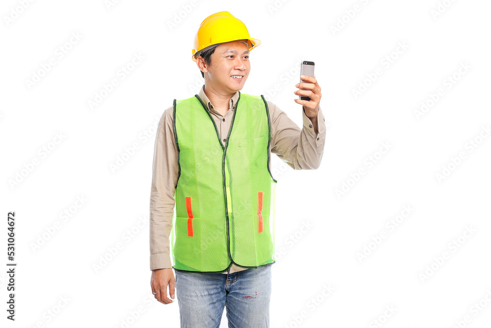 Young Asian engineer in yellow safety helmet using mobile phone to make a call standing on white background