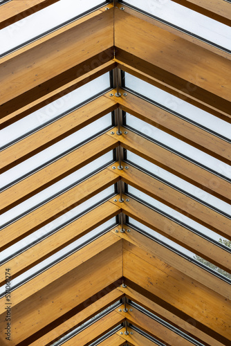 Exposed wooden truss rafters supporting glass skylight roof in modern eco-friendly building ceiling.
