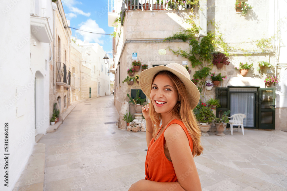 Beautiful young joyful woman smiling and looking at camera. Portrait of young tanned woman with hat and orange dress enjoying her summer holidays in Italy.
