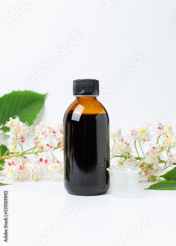 Bottle of horse chestnut extract, essence of chestnut flowers. Flowering branches and leaves of horse chestnut.