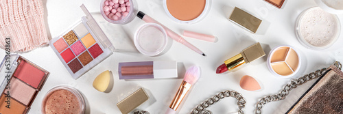 Autumn make up set on white table background, with autumn leaves and beauty accessories. Various makeup professional cosmetics on white table background with fall cozy sweater and woman handbag