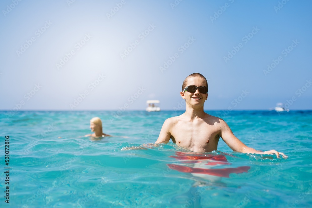 Child boy with swimming goggles swims in the sea next to a rock during a happy summer vacation in Corfu, Greece