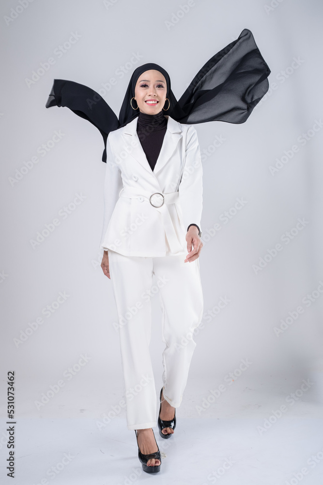 Portrait of a beautiful female model wearing hijab, a lifestyle apparel for Muslim women isolated on grey background. Idul Fitri and hijab fashion concept. Portrait of a beautiful female model wearing hijab, a lifestyle apparel for Muslim women isolated on grey background. Idul Fitri and hijab fashion concept.
