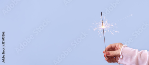 sparklers in a woman's hand on a blue background with copy space. Christmas holiday concept