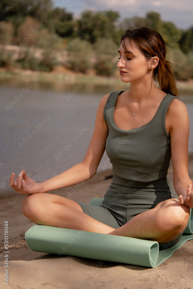A girl in sportswear does yoga on the street, a girl goes in for sports on the street, dressed in a green tracksuit, sports in nature, doing yoga near the water, sports lifestyle