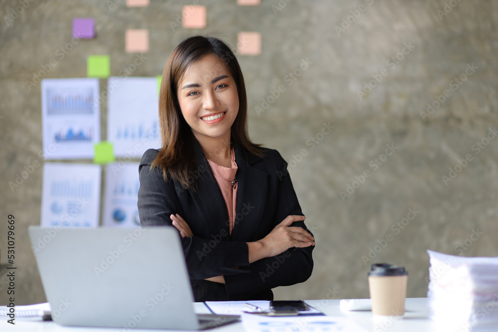 Portrait of a charming Asian businesswoman in the office looking at the camera while working on a computer laptop. Portrait of a charming Asian businesswoman in the office looking at the camera while working on a computer laptop.