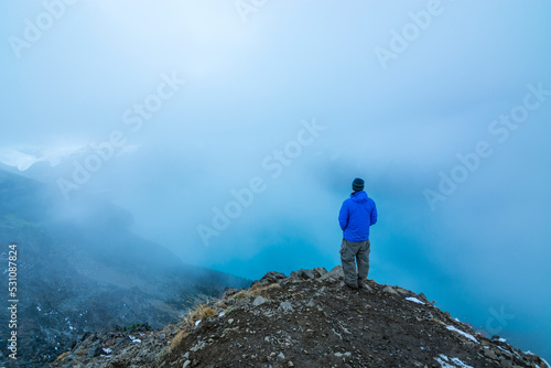 Adventurous athletic male hiker standing at the summit of Panorama Ridge looking down at Garibaldi Lake on a cloudy day.  © Pelo Blanco Photo
