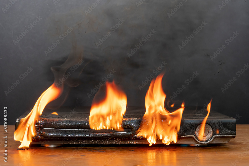 Obraz premium A DVD player is burning on the table, flames are rising up, the case has melted, a fire has started in the apartment.