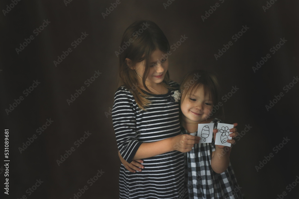 Funny Sisters Girls With Painted Toys On A Dark Background, Concept Childhood And Sublimation - obrazy, fototapety, plakaty 