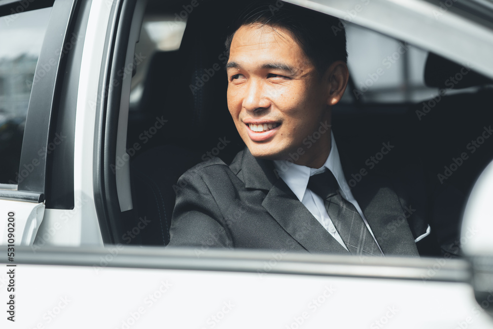 Close-up photo of an Asian man in a formal suit sitting in a car, traveling by car, safe driving, respecting traffic rules.
