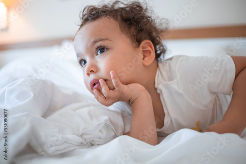 Funny curly toddler lying on the bed and attentively watching TV