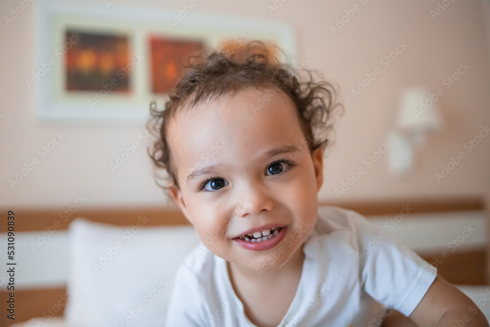 Happy smiling toddler boy on the bed looking to camera