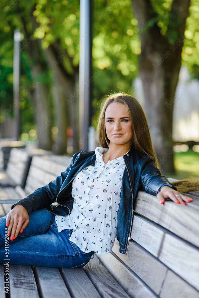 A beautiful fashion young city woman sitting on a bench.Summer,autumn day. A beautiful fashion young city woman sitting on a bench.Summer,autumn day.