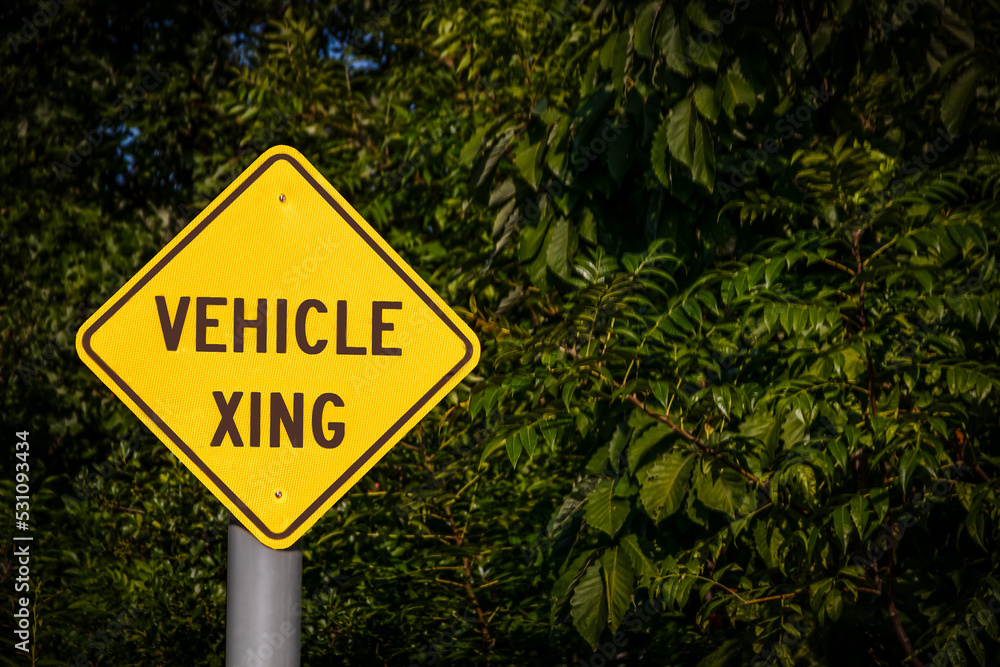 Closeup - Yellow Vehicle Xing Sign against dark green foliage