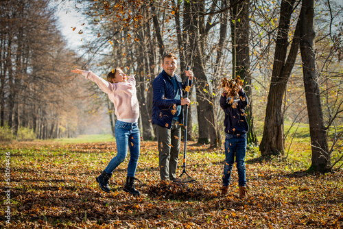 Father raking autumn leaves while his children playing and jumping around