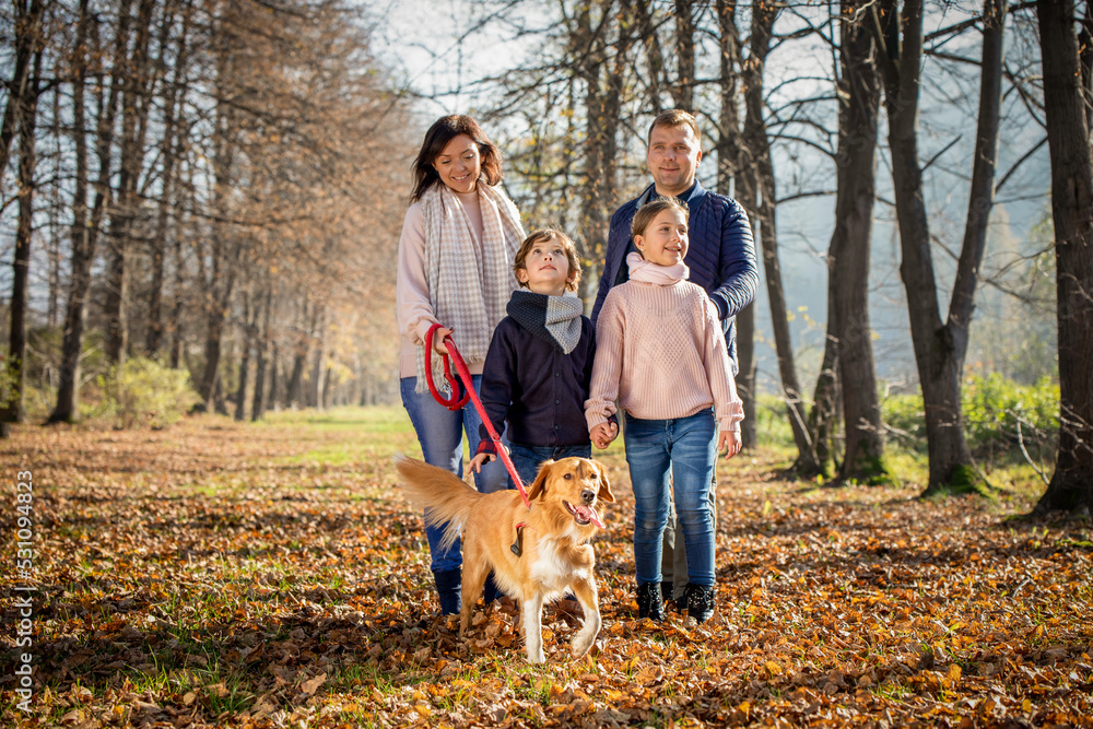 Happy family with dog walking in the autumn park among yellow leaves