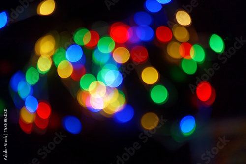 Defocused bokeh lights on black background, an abstract naturally blurred backdrop for Christmas eve or birthday party. Festive light texture. Colorful garland in blur. Overlay effect for design. 2023 © Lavsketch