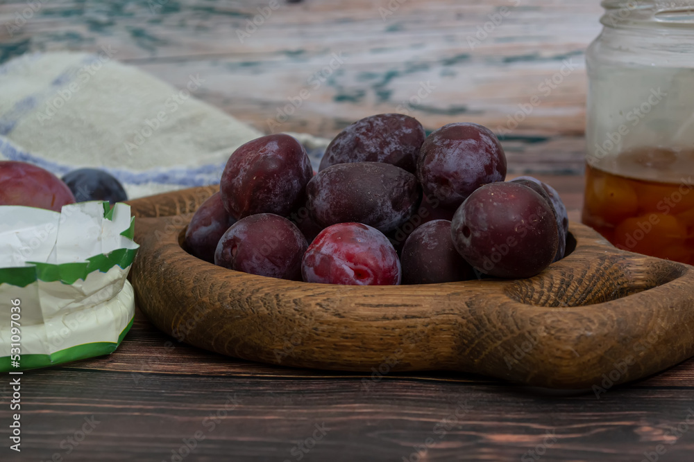 Obraz premium A bowl of fresh blue plums on a wooden background.