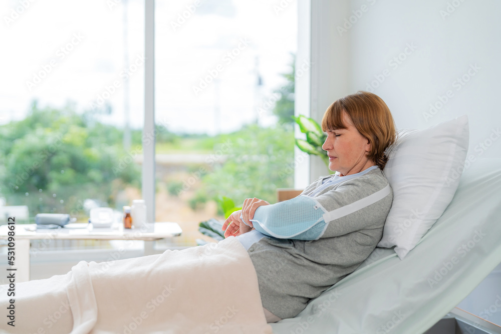 Elderly patient woman lying on bed wearing broken arm support at