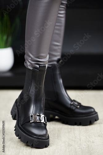 Young woman in leather pants trying on black boots in the shop, copy space. Woman wearing comfortable stylish boots indoors, closeup.