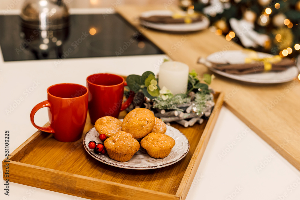 On the table is a plate of muffins, two red cups and a candle. New Year On the table is a plate of muffins, two red cups and a candle. New Year